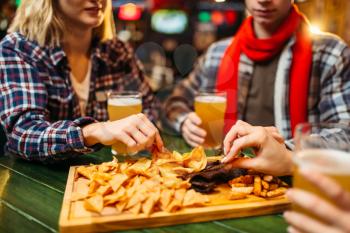 Football fans drinks beer and eats chips at the table in sports bar. Victory celebration, tv broadcasting, young friends leisures in pub