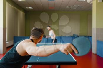 Man and woman playing ping pong indoors, focus on racket. Couple in sportswear plays table tennis in gym