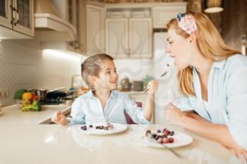 Young mother with her kid tastes chocolate pastry. Cute woman and little boy cooking on the kitchen. Happy family tasting sweet dessert at the counter and having fun
