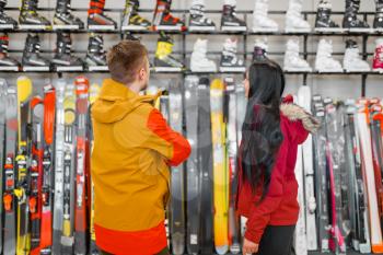 Couple at the showcase choosing skiing or snowboarding equipment, shopping in sports shop. Winter season extreme lifestyle, active leisure store, customer buying ski