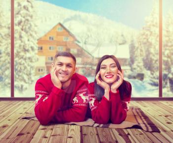 Happy love couple lies on the floor, christmas holidays. Xmas celebration, cheerful man and woman in red pullovers, snowy mountain village on background