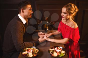 Beautiful love couple in restaurant, romantic evening. Elegant woman in red dress and her man sitting at the table, anniversary celebration