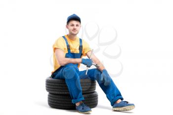 Car tire service, worker in blue uniform sitting on car tyres, white background, repairman, wheel mounting