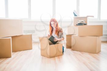 Smiling woman sitting on the floor among cardboard boxes, housewarming. Relocation to new home