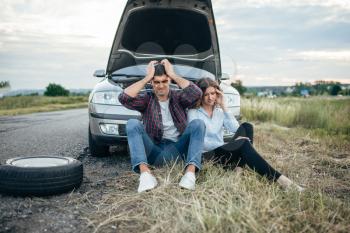 Tired man and woman sitting against broken car with open hood. Trouble with vehicle on road in summer day