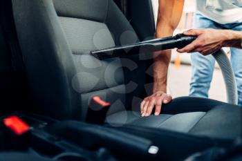 Man cleans car interior with vacuum cleaner on carwash station. Automobile cleaning