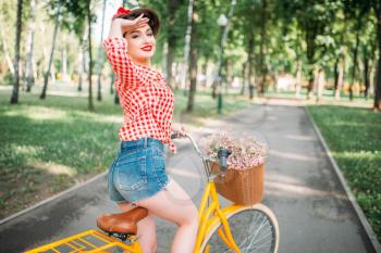 Pinup girl on retro bicycle with backet of flowers. Pin-up style pretty woman