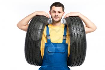 Tire service worker in blue uniform holds car tyres in hands, white background, repairman, wheel mounting