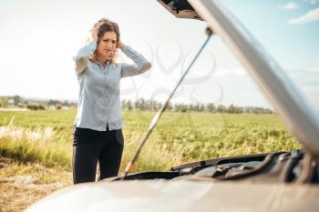Depressed woman looking at motor, broken car with open hood. Trouble with vehicle