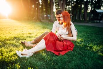 Love couple sits on a grass in summer park. Romantic date of attractive woman and young man