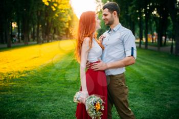 Beautiful love couple hugs on sunset, romantic meeting outdoors. Attracrive woman with flowers and young man leisure together in park