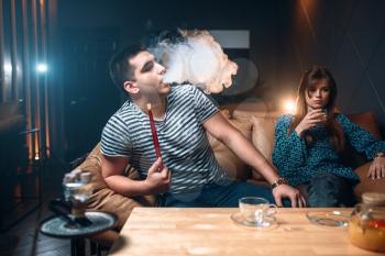 Young couple relax and smoking hookah, tobacco smoke at night bar