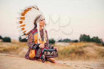 American Indian woman sitting in yoga pose. Headdress made of feathers of wild birds. Cherokee, Navajo culture, ethnic peoples traditions