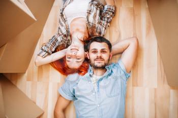 Smiling couple lies on the floor among cardboard boxes, top view, moving to new house, housewarming