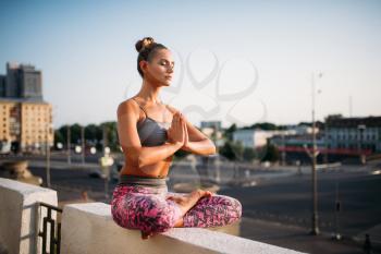 Beautiful young woman relax in yoga pose, city on background. Yogi meditation exercise outdoors