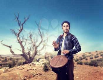 Young male drummer plays on wooden bongo drums in desert, musician in motion. Djembe, musical percussion instrument, ethnic music