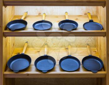 Frying pans on wooden shelf, cooking tools. Kitchen decoration, iron utensil