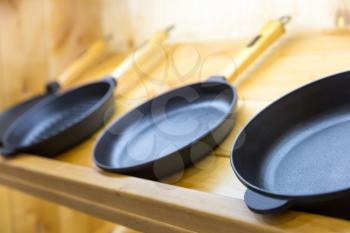 Frying pans on wooden shelf closeup, cooking tools. Kitchen decoration, iron utensil