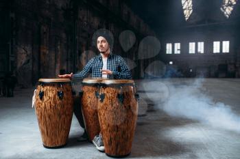 Male drummer plays on wooden drums in factory shop, musician in motion. Bongo, musical percussion instrument, ethnic music