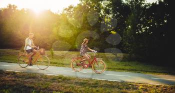 Love couple riding on vintage bicycles in summer park, romantic date of young man and woman. Boyfriend and girlfriend together outdoor, retro bike