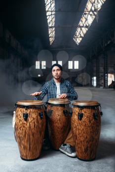 Male drummer playing on wooden bongo drums in factory shop, musician in motion. Djembe, musical percussion instrument, ethnic beat music