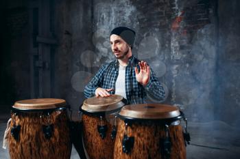 Drummer playing on wooden bongo drums in factory shop, beat rhythm, musician in motion. Djembe, musical percussion instrument