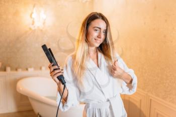 Beautiful woman with curling iron, bathroom on background. Bodycare and hygiene, healthcare