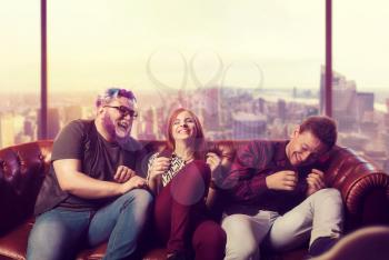 Home party, cheerful friends sitting on the couch and laugh. Happy friendship, threesome ha-ha on sofa, cityscape on background