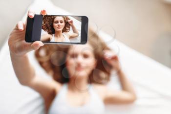 Attractive woman in underwear lies in bed and makes selfie on phone. Girl wake up in the morning
