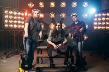 Musical group poses on the stage with lights in night club, vintage style. Guitarists and drummer, rock band concert, music show and entertainment