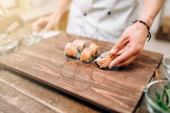Male person cooking sushi on wooden table, japanese kitchen preparation process. Traditional asian cuisine, seafood delicious