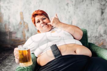 Overweight woman sitting in chair and drinks beer, bulimic, obesity. Unhealthy lifestyle, fatty female