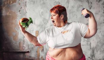 Overweight woman with dumbbell and sandwich in hands, fight against obesity concept, overweight problem. Junk food eating