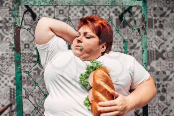 Fat woman with sandwich in hands liying on the bed, bulimic and overweight. Unhealthy lifestyle, obesity