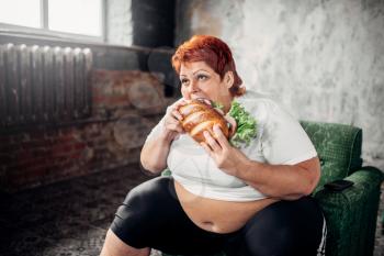 Overweight woman sits in a chair and eats sandwich, bulimic. Unhealthy lifestyle, obesity