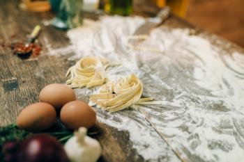 Ingredients for cooking homemade pasta on wooden kitchen table sprinkled with flour closeup, nobody. Fettuccine preparation