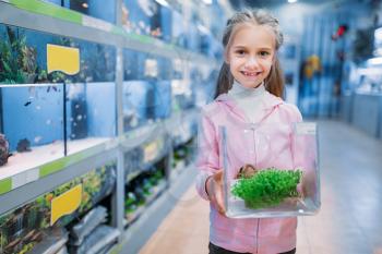 Little girl with plant for aquarium in pet shop. Kid chooses element of flora for her fishbowl in petshop