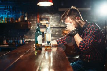 Alcoholic sitting at the bar counter and drinks strong alcohol beverages. Male person in pub, alcoholism,  drunkenness