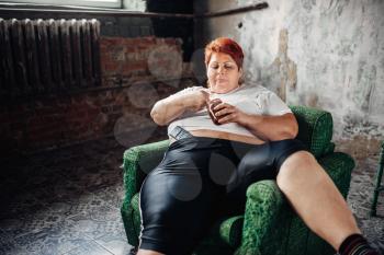 Overweight woman sits in a chair and eats sweets. Unhealthy lifestyle, obesity