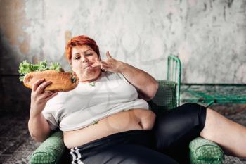 Fat woman sits in a chair and eats sandwich, overweight, fatty and bulimic. Unhealthy lifestyle, obesity