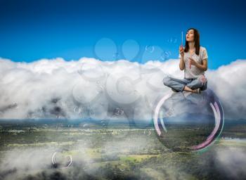 Cute woman flying in the sky on big soap bubble. Female person blowing colorful balloons