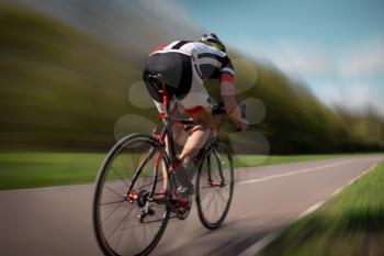 Cyclist in helmet and sportswear rides on bicycle, speed effect, back view. Workout on bike path, cycling