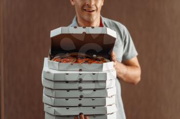 Delivery man shows fresh pizza in box, delivering service. Courier from pizzeria holds cardboard packages indoors