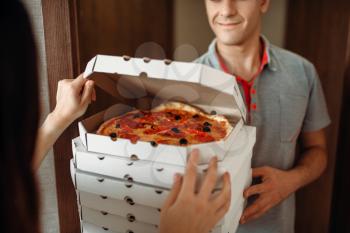 Delivery man shows fresh and hot pizza to female customer at the door, delivering service. Deliver from pizzeria and woman near the entrance to the apartment, pizzaman and buyer