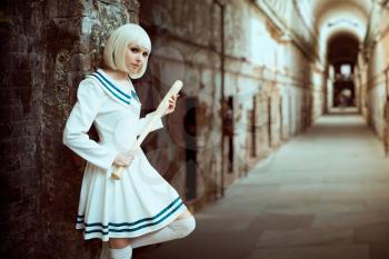 Anime girl with baseball bat. Cosplay fashion, asian culture, doll in uniform, cute woman with makeup in an abandoned factory shop