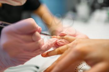 Beautician in pink gloves applying nail varnish to female client, manicure in beauty salon. Manicurist doing hands care cosmetic procedure