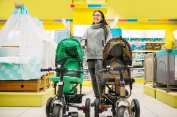Pregnant woman poses with strollers in childrens goods store. Future mother choosing pushchair for her child