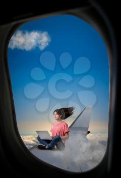 PC addiction, woman with laptop sitting on plane wing, view from airplane porthole