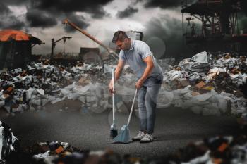 Man with a scoop and a broom sweeps on a garbage dump. Useless or pointless activity concept