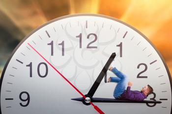 Man lies on the arrow of a huge clock and trying to stop time. Deadline concept